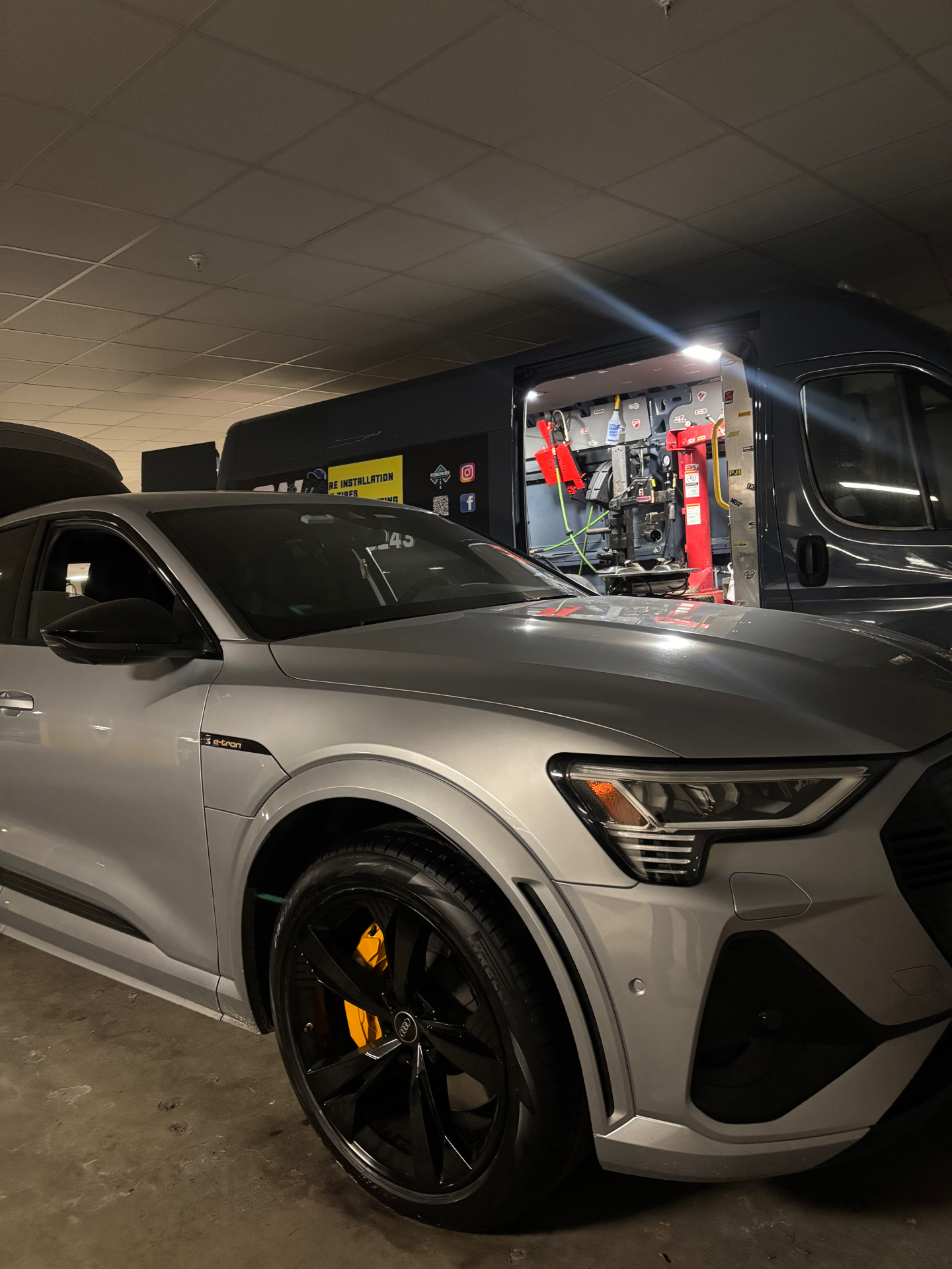 Audi e-tron with yellow brake calipers being serviced next to the On-Site Mobile Tire van with tire machine inside