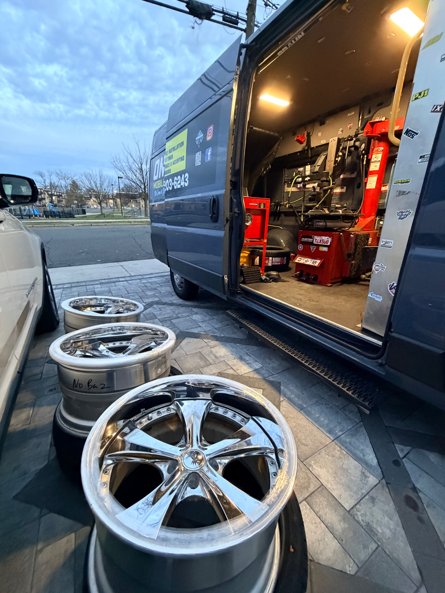 Set of large chrome wheels lined up next to the On-Site Mobile Tire van with tire machine inside